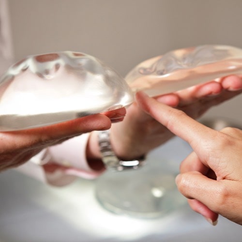 Image of one person holding a clear implant in each hand and a second person pointing to one of the implants.